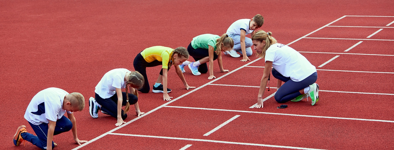 vrouw coacht groep jongeren op atletiekplein