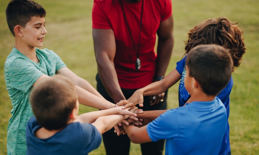 jongens en coach doen een huddle op het sportveld